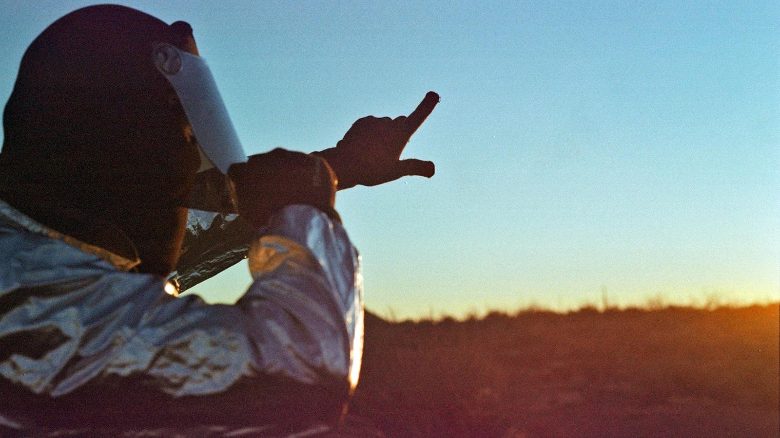 A person in a reflective suit points toward the horizon at sunset across an open landscape. The scene aligns with the Weather Supply Company’s perspective that climate challenges demand broader approaches, incorporating geoengineering and localized weather modification into conversations about the future of environmental systems.